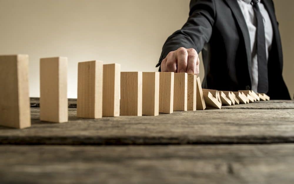 Businessman stopping domino effect with his finger. Business solutions concept.